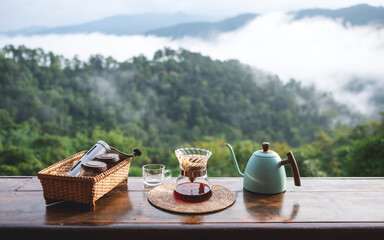 A set of coffee drip equipment on wooden balcony with mountain and nature view on foggy day
