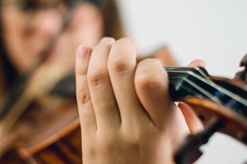 close up female hand on violin fingerboard making a note, with blurred background, focus on hand.