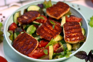 Grilled halloumi cheese served on vegetable salad with tomato, cucumber and lettuce on the plate