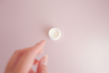ピンクの背景に置かれた白い容器に入ったクリームを手に取ろうとしてる女性の手元の写真素材
