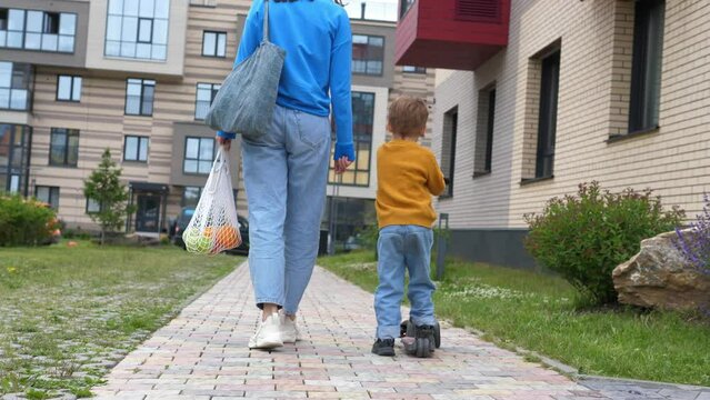 Rear view of a happy mother and son walking home after a joint grocery shopping trip to the supermarket.