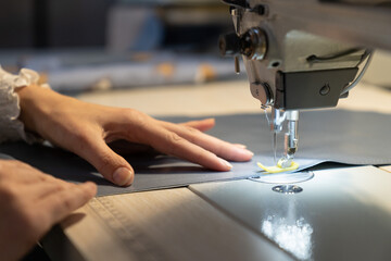 Woman tailor work on sewing machine stitching patterns of new collection. Closeup shot of female sewer hand dressmaking. Seamstress use professional equipment for tailoring. Garment industry concept