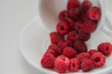 Juicy ripe raspberries in a white cup on a white background. Selective focus.