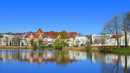 Fototapeta na wymiar schöner Blick über spiegelnden Burgsee auf Häuser in Schwerin mit Bäumen unter blauem Himmel