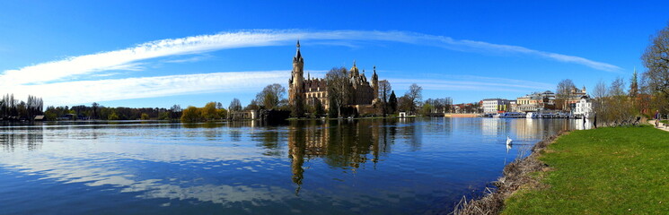 Fototapeta na wymiar weites Panorama vom Schweriner Schloss im See mit grüner Wiese und weißen Wolken am blauen Himmel