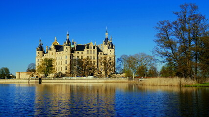 Obraz premium prächtiges Schloss in Schwerin am Burgsee am Abend neben Schilf und Bäumen unter blauem Himmel