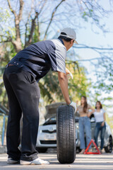 Naklejka premium Expertise mechanic man in uniform holding a tire for help a woman for changing car wheel on the highway, car service, repair, maintenance concept.