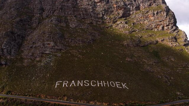 Name of Franschhoek laid out in white stones on rugged mountainside; aerial