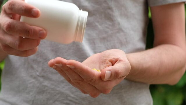 Close up shot of a man pouring yellow pills from white plastic bottle into hand. Slow motion.