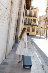 young smiling woman in dress walking with suitcase on street in valencia.