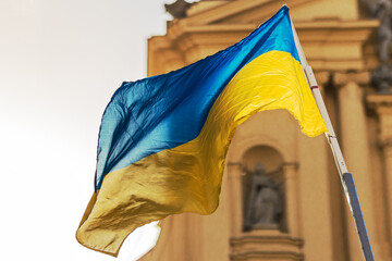 Flag Ukraine waving in the wind against the city on Church Background. Support Ukraine in Europe. Stand with Ukraine. Ukraine Flag Backlight on Church Background in Germany.