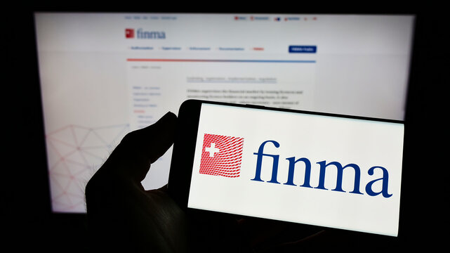Stuttgart, Germany - 06-04-2022: Person holding mobile phone with logo of Eidgen&ouml;ssische Finanzmarktaufsicht (FINMA) on screen in front of web page. Focus on phone display.
