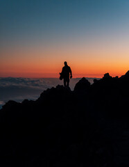 Silhouette of the person on top of the rocks during sunset on the peak of Mount Teide called 'Pico del Teide'. Teide National Park, Tenerife, Canary islands, Spain.