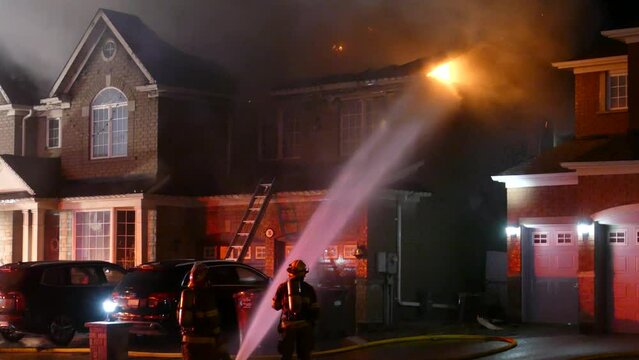 firefighters extinguish fire, spraying house with hose at night.. Burning house fire firefighters fighting a huge blaze of fire burning house. house on fire nighttime