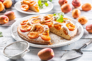 Apricot pie on a white plate, apricots, mint and powdered sugar on the kitchen table