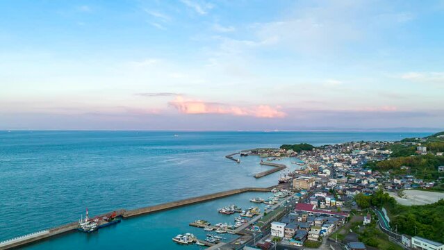 Aerial time lapse over small fishing town with sunset clouds in background
