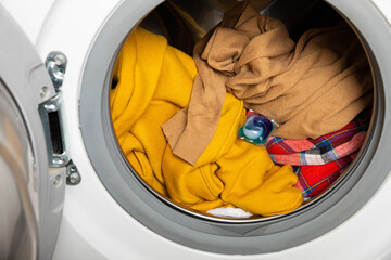  laundry detergent capsule into washing machine indoors, closeup.Colorful laundry eco gel in...