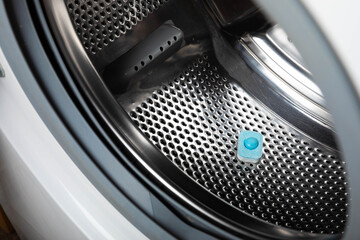 Capsule with liquid powder in the washing machine with laundry, close-up. Gel for washing in the car. Colorful eco-gel for washing in capsules. Washing clothes. Purity concept