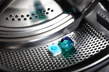 Capsule with liquid powder in the washing machine with laundry, close-up. Gel for washing in the...