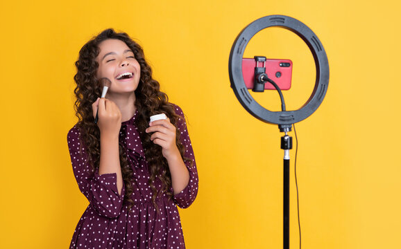 laughing girl with long curly hair making video for blog hold powder brush