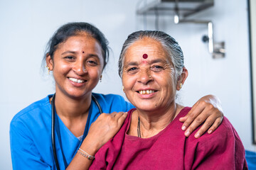 Happy smiling nurse hugging or embracing senior sick women by looking camera at hospital bed -...