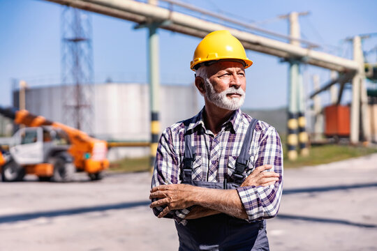 An experienced senior factory worker standing in a refinery yard and looking away.