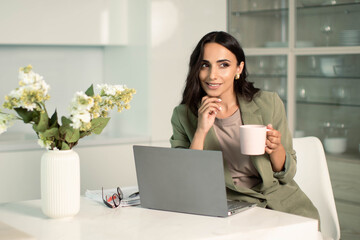 Business woman using laptop computer indoors at home office, with notes on papers, holding mug of coffee or tea, remote work and  freelancer, education and student, shopping online and application use