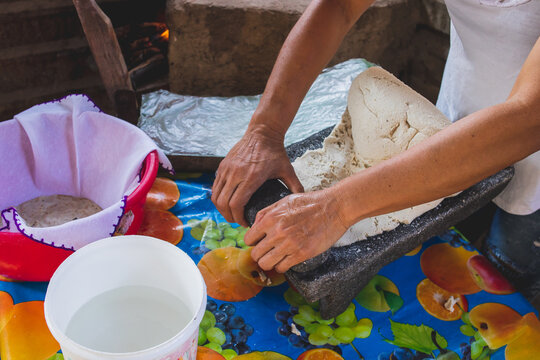 Mujer mexicana torteando maza de maíz en un metate y una estufa de leña para hacer tortillas caseras	
