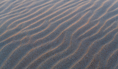 Fototapeta na wymiar Sand ripples texture with waves at sunset as background or wallpaper.