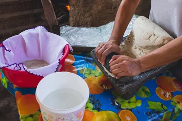 Foto op Canvas Mujer mexicana torteando maza de maíz en un metate y una estufa de leña para hacer tortillas caseras   © JP STUDIO