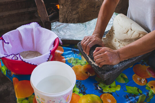 Mujer mexicana torteando maza de maíz en un metate y una estufa de leña para hacer tortillas caseras	
