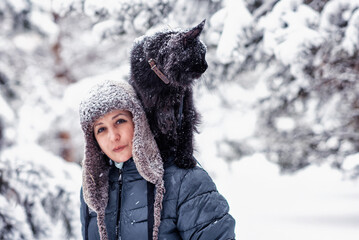 A woman carring a big black maine coon cat in a snowy Siberian forest on a frosty day. Concept: winter.