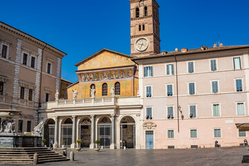 The basilica of Santa Maria in Trastevere, in a square of the  center of Rome. The facade with the portico and the mosaic, the bell tower with the clock and the fountain with the inscription SPQR.