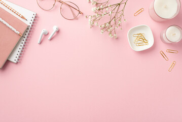 Fototapeta na wymiar Business concept. Top view photo of workspace candles notepads clips pencils stylish glasses earbuds and white gypsophila flowers on isolated pastel pink background with copyspace