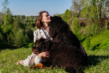 Smiling woman in casual clothes sitting on grass with tibetan mastiff dogs and playing together outdoors