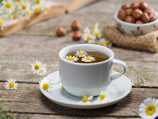 Healthy chamomile tea and chamomile herbs on wooden table. Books and nuts in the background....