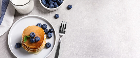 Plate of tasty pancakes with blueberries and honey on light grey table, flat lay with space for...