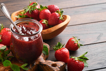 Strawberry jam. Strawberry jam in glass jar with fresh berries plate on an old wooden dark table background, closeup. Homemade strawberry fruity jam. Top view with copy space.