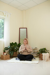 Calm relaxed woman crossing legs while sitting on rug in lotus position during meditation
