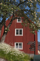 Façade of a red wood building, a pool with directions signs on the island Beckholmen a sunny summer day in Stockholm