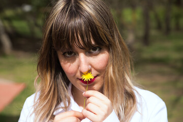 Portrait of young, beautiful, blonde woman in white shirt smelling a small yellow daisy. Concept beauty, plants, flowers, spring, summer.