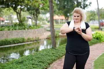 Plus size young woman checking fitness tracker after running outdoors