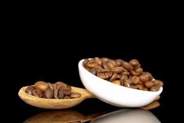 Roasted aromatic coffee beans in a ceramic white saucer with a wooden spoon, close-up, isolated on a black background.