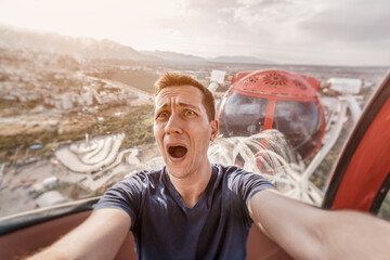 A guy with acrophobia or fear of heights screams with funny emotions on his face from the view from...