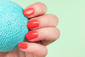 Female hand with beautiful bright summer manicure - coral, red orange nails against mint green...