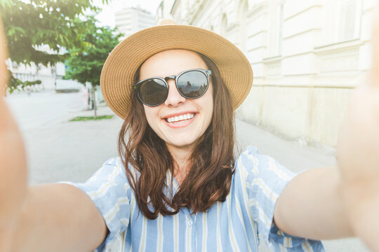 Happy young woman wearing sunglasses and sun hat taking a selfie.