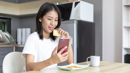 Asian woman eats breakfast with crackers (Healthy whole grain) and juice, Use your phone or mobile phone to search for morning news, Small room in condominium background, Wake-up activities.