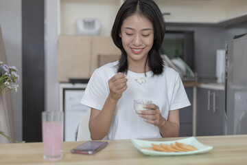 Half-Japanese woman eats yoghurt with cereal for breakfast in room, Healthy food and digestive system maintenance, The most popular and easy to eat breakfast food.