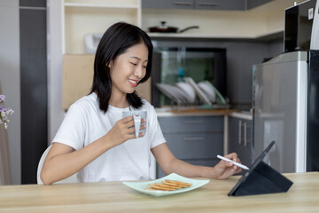 Asian woman eats breakfast with crackers (Healthy whole grain) and juice, Use your phone or tablet to search for morning news, Small room in condominium background, Wake-up activities...