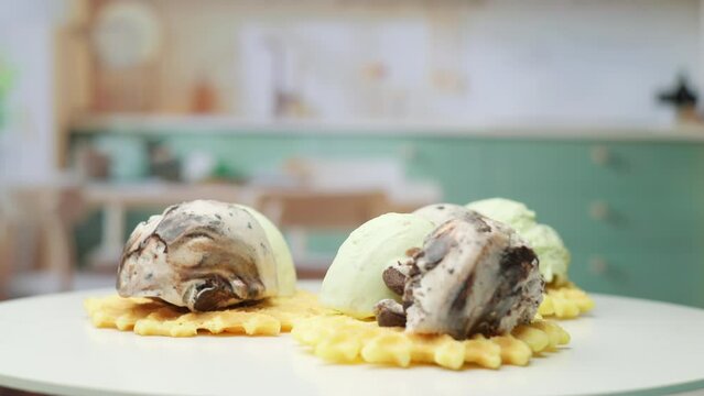 Waffles with pistachio and chocolate ice ream balls on top rotating in the kitchen in slow motion.